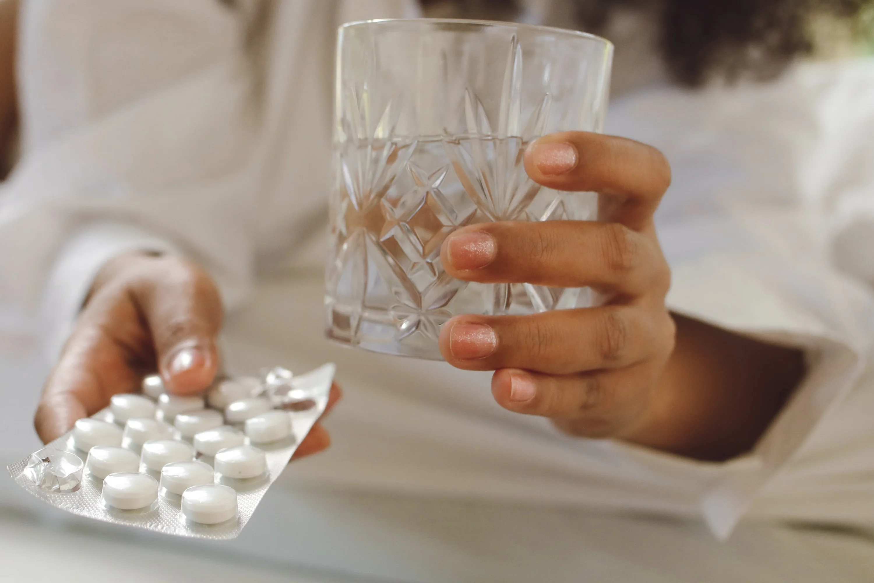 a person holding a packet of medication and a glass of water